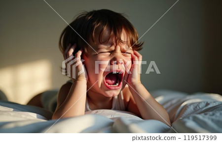 A small boy is crying quietly while lying atop a bed in distress A small boy is crying quietly while lying atop a bed in distress 119517399