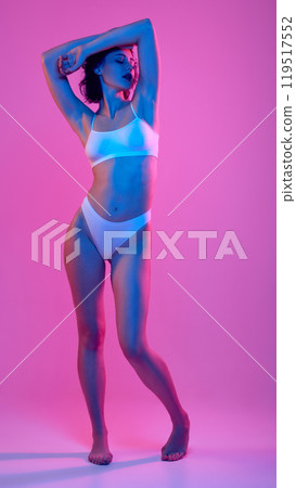 Woman posing elegantly with her arms raised, gracefully accentuating her curves in neon light against vibrant, colorful backdrop. Woman posing elegantly with her arms raised, gracefully accentuating her curves in neon light against vibrant, colorful backdrop. 119517552