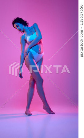 Woman stands in white underwear, elegantly posing with her body in vibrant neon hues of blue and pink, against gradient background. Woman stands in white underwear, elegantly posing with her body in vibrant neon hues of blue and pink, against gradient background. 119517556