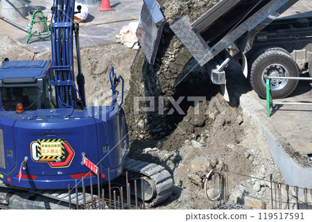 Construction site of new apartment building: Backfilling with soil using a backhoe 119517591