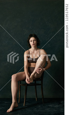 Young woman sits on chair in relaxed pose, showing thoughtful expression while barefoot, promoting body positivity 119517652