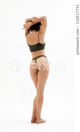 Rear view photo of young woman in dark green underwear raising hands and showing her fit curves against white studio background. Rear view photo of young woman in dark green underwear raising hands and showing her fit curves against white studio background. 119517731