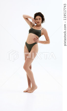 Fit, attractive female model radiates confidence in her dark green lingerie, standing tall against white studio background. Fit, attractive female model radiates confidence in her dark green lingerie, standing tall against white studio background. 119517743