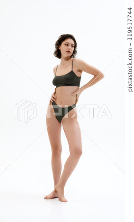 Full-body photo of young attractive woman posing elegantly dressed in dark green underwear against white studio background. 119517744