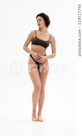 Confident young and fit woman in dark green minimalist underwear set strikes relaxed pose. Effortless style and grace. 119517748