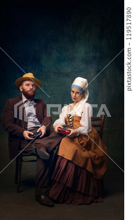 Creative portrait of elegant couple in vintage-inspired clothes sitting at table and playing with gaming controllers. Creative portrait of elegant couple in vintage-inspired clothes sitting at table and playing with gaming controllers. 119517890