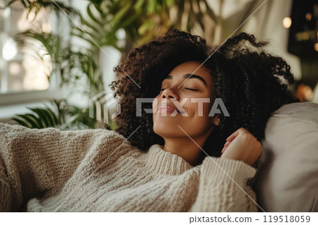 A woman relaxes comfortably in a cozy sweater while enjoying peaceful moments indoors surrounded by 119518059
