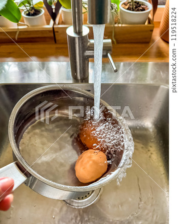 two Cooling boiled eggs under running water in a stainless pan after cooking. High quality photo two Cooling boiled eggs under running water in a stainless pan after cooking. High quality photo 119518224