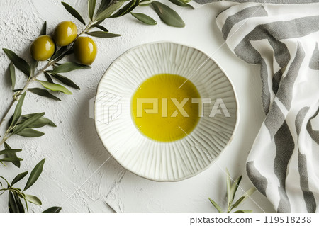 Freshly poured olive oil in a textured dish beside green olives and a striped napkin on a light Freshly poured olive oil in a textured dish beside green olives and a striped napkin on a light 119518238