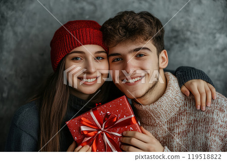 Happy couple celebrating together while holding a wrapped gift in cozy winter attire against a 119518822