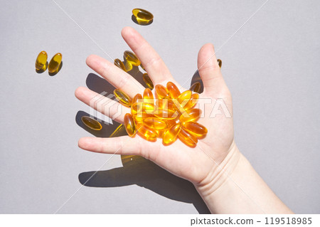 Hand holding omega 3 capsules against gray background highlighting health Hand holding omega 3 capsules against gray background highlighting health 119518985