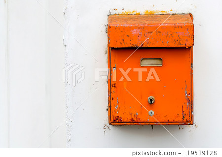 An old, weathered orange mailbox mounted on a white wall, showcasing the effects of time and the 119519128