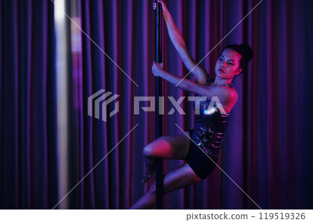 Skilled Pole Dancer Performing Under Neon Lights 119519326
