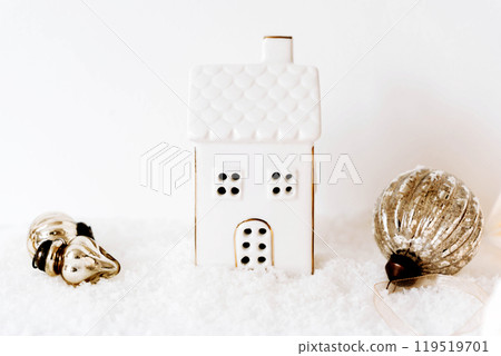 Small white ceramic house candle holder with gold Christmas decorations on soft white faux snow 119519701