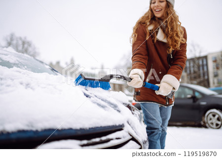 Beautiful woman is cleaning snow from a car with a brush. Transport concept, seasonality 119519870