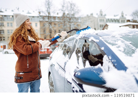 Beautiful woman is cleaning snow from a car with a brush. Transport concept, seasonality 119519871
