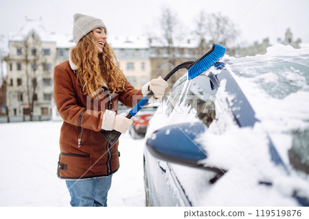 Portrait of young woman cleaning snow off car during winter snowfall. Winter, vehicle concept. Portrait of young woman cleaning snow off car during winter snowfall. Winter, vehicle concept. 119519876
