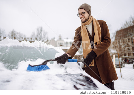 Transport, winter, weather, people and vehicle concept - young man cleaning snow from car with brush 119519959