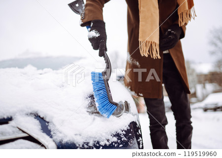 Transport, winter, weather, people and vehicle concept - young man cleaning snow from car with brush 119519960