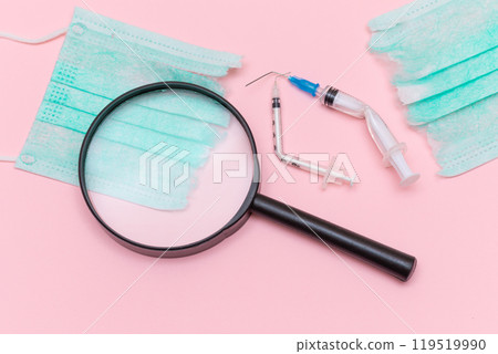 Broken Medical Syringe and Green Torn Medical Face Mask with Magnifying Glass 119519990