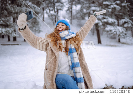Portrait of a beautiful woman in warm clothes takes selfie with a hot drink from a thermos in hands. 119520348