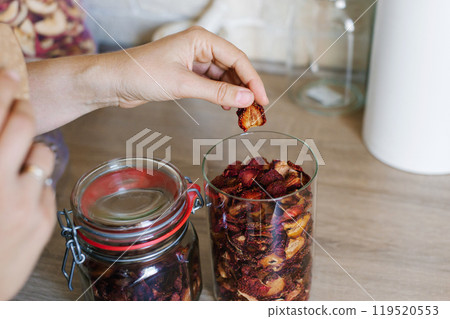 Woman Organizes Dried Fruit in Glass Jars on Kitchen Countertop 119520553