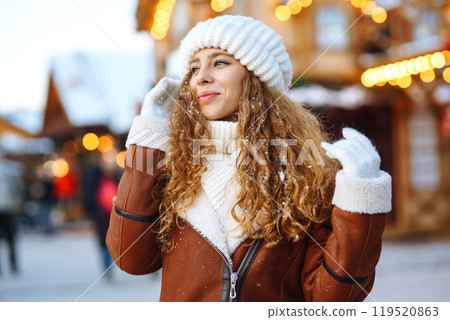 A young woman walks through a Christmas market decorated with festive decorations and lights. 119520863