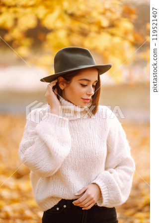Autumn woman. Young cheerful woman in white sweater and hat walks in the nature park on a sunset. Autumn woman. Young cheerful woman in white sweater and hat walks in the nature park on a sunset. 119521407
