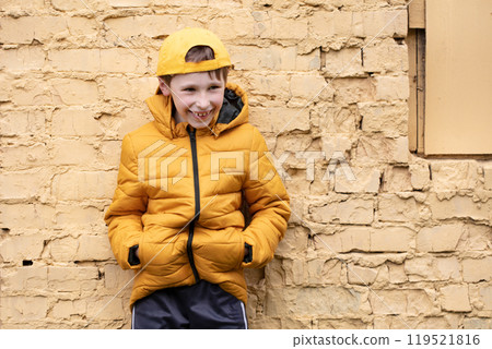 A child on the street. A happy boy is standing against a brick wall in yellow clothes and a baseball cap. A child on the street. A happy boy is standing against a brick wall in yellow clothes and a baseball cap. 119521816