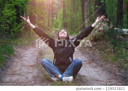 Man in the forest. A middle-aged woman sits on a forest road lit by the sun. 119521821