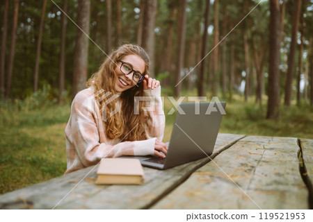 Beautiful woman working online or studying at laptop sitting at park. Freelance, education concept. Beautiful woman working online or studying at laptop sitting at park. Freelance, education concept. 119521953