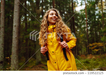 Traveler woman in yellow coat explores, walks through wild forest in nature. Vacation travel concept 119522125