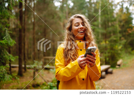 Travel apps. Curly young woman traveler in yellow coat holding smartphone in hand. Concept of travel 119522153