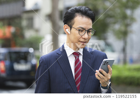A businessman in his late 30s wearing earphones looking at his smartphone 119522155