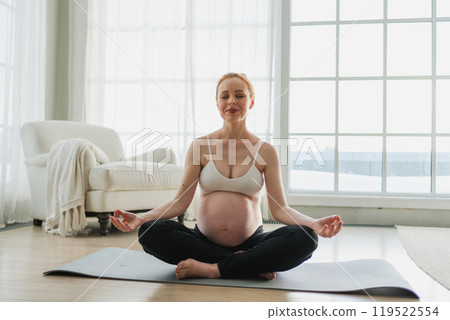 Pregnancy prenatal breathing. Pregnant woman with big belly sitting in lotus pose on yoga matt at home. Pregnant girl practicing yoga mindfulness meditation. Relaxation self care during pregnancy 119522554