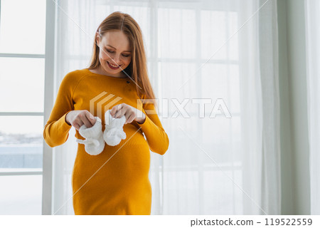 Pregnancy motherhood people expectation future. Pregnant woman with big belly holding newborn baby booties smiling at home. Young mom enjoying pregnancy. Maternity tenderness parenthood new life 119522559