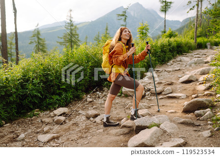 Traveler with hiking poles, bright backpack enjoys mountain scenery along hiking trail. Wanderlust. 119523534