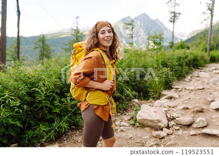Woman traveler with yellow hiking backpack, hiking poles on trail among mountains. Adventure concept 119523551