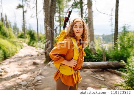 Woman traveler with yellow hiking backpack, hiking poles on trail among mountains. Adventure concept 119523552