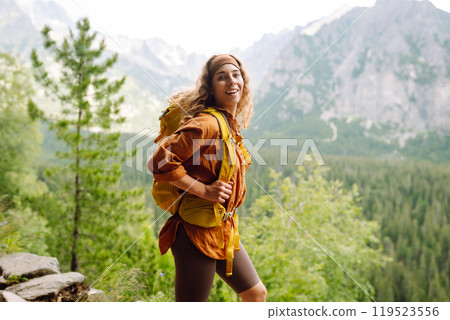Happy woman with a yellow hiking backpack enjoying the mountain landscape. Travel concept. 119523556
