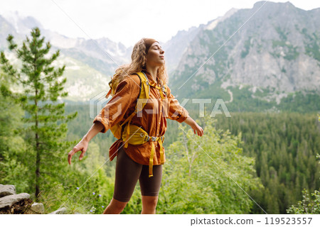 Happy woman with a yellow hiking backpack enjoying the mountain landscape. Travel concept. 119523557