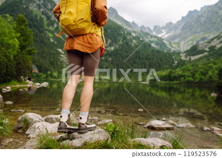 Female traveler with yellow hiking backpack against the backdrop of mountain lake with hiking poles. Female traveler with yellow hiking backpack against the backdrop of mountain lake with hiking poles. 119523576