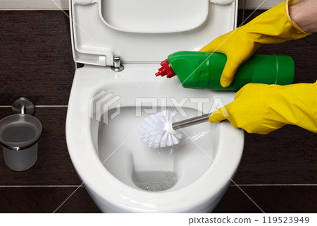 cleaning a toilet with a toilet brush and disinfectant in a bathroom with dark tiles cleaning a toilet with a toilet brush and disinfectant in a bathroom with dark tiles 119523949