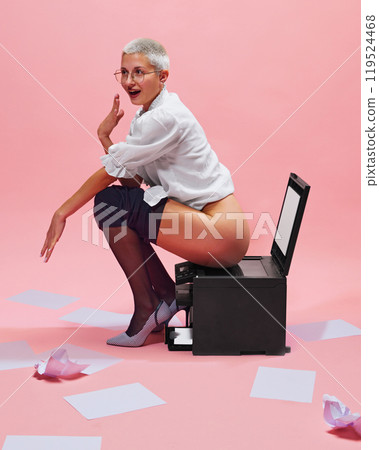 Humorous photography with young woman, office worker sitting on printer in unusual way Humorous photography with young woman, office worker sitting on printer in unusual way 119524468