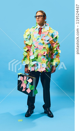 Determined office worker covered in sticky notes. Young man, employee in formal wear standing against blue background 119524487