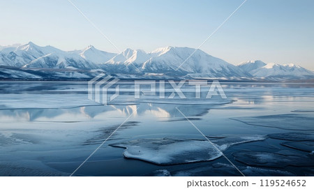 Tranquil photo capturing a frozen lake in the foreground with majestic, snow-capped mountains reflecting in the ice 119524652