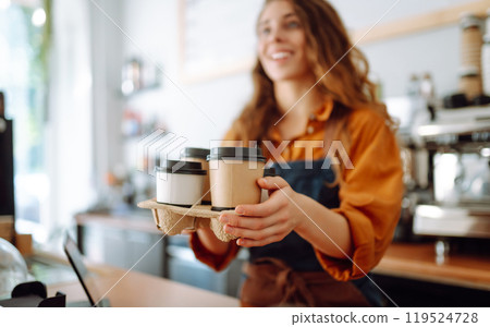 Young female barista holding disposable glasses with hot drink to go. Takeaway delivery concept. Young female barista holding disposable glasses with hot drink to go. Takeaway delivery concept. 119524728