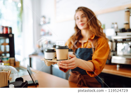 Young female barista holding disposable glasses with hot drink to go. Takeaway delivery concept. Young female barista holding disposable glasses with hot drink to go. Takeaway delivery concept. 119524729