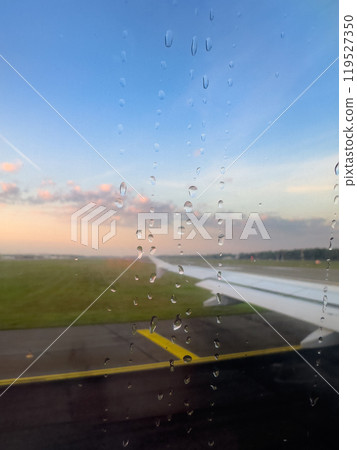 Rain Droplets on Airplane Window With View of Runway at Sunset During Departure From Airport 119527350