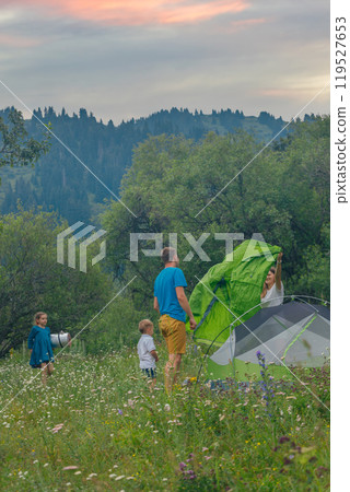 A joyful family is enjoying a delightful camping experience, setting up a bright tent in a scenic landscape A joyful family is enjoying a delightful camping experience, setting up a bright tent in a scenic landscape 119527653